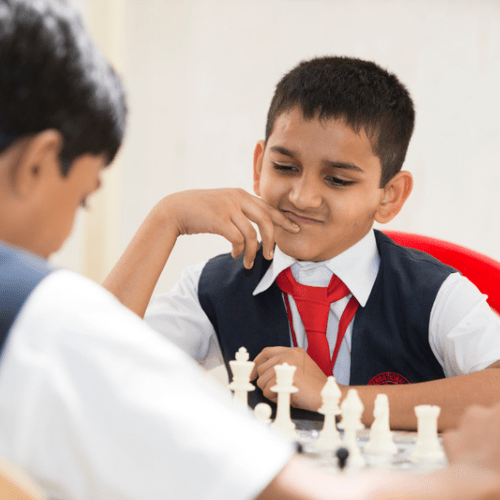 Two boys engrossed in a game of chess during playtime at Panbai International School. One boy is contemplating his next move with his hand on his chin, displaying a strategic mindset