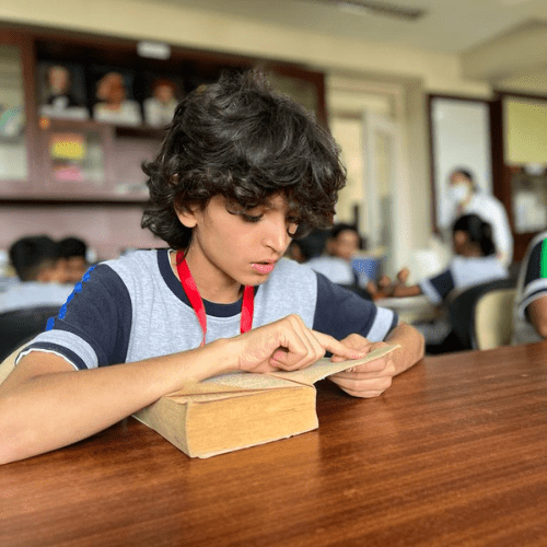 A boy engaged in reading a book at the Panbai International School library, using his hands to scroll through the words, absorbed in his reading