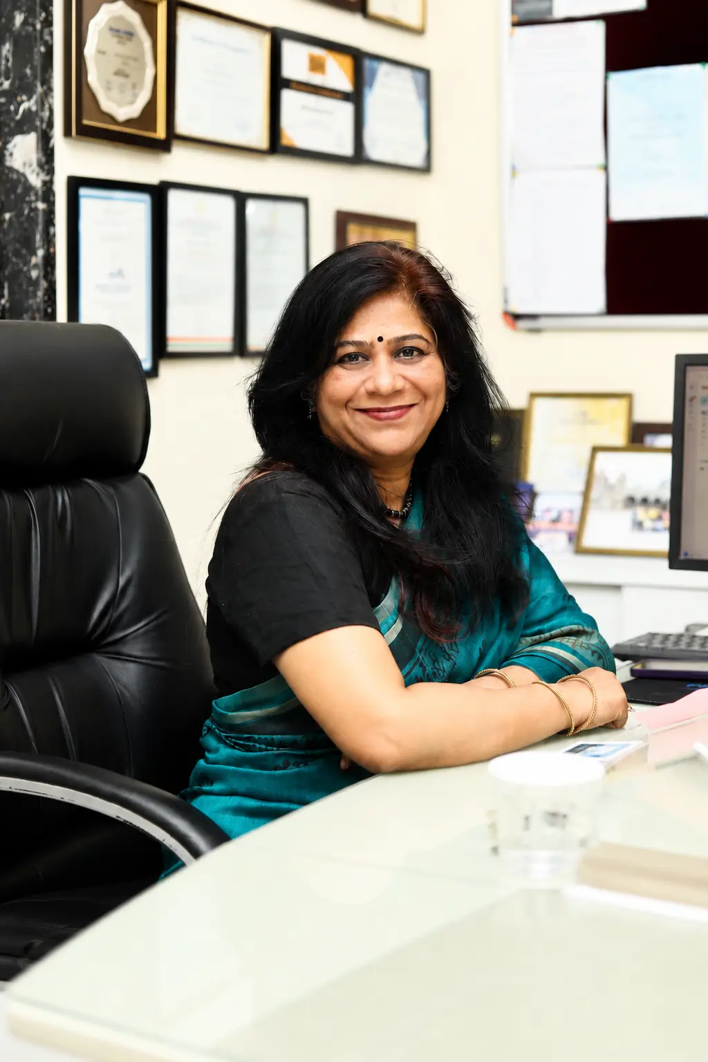 Principal of Panbai International School sitting in her office, smiling at the camera in a professional portrait setting with certificates and workspace in the background.